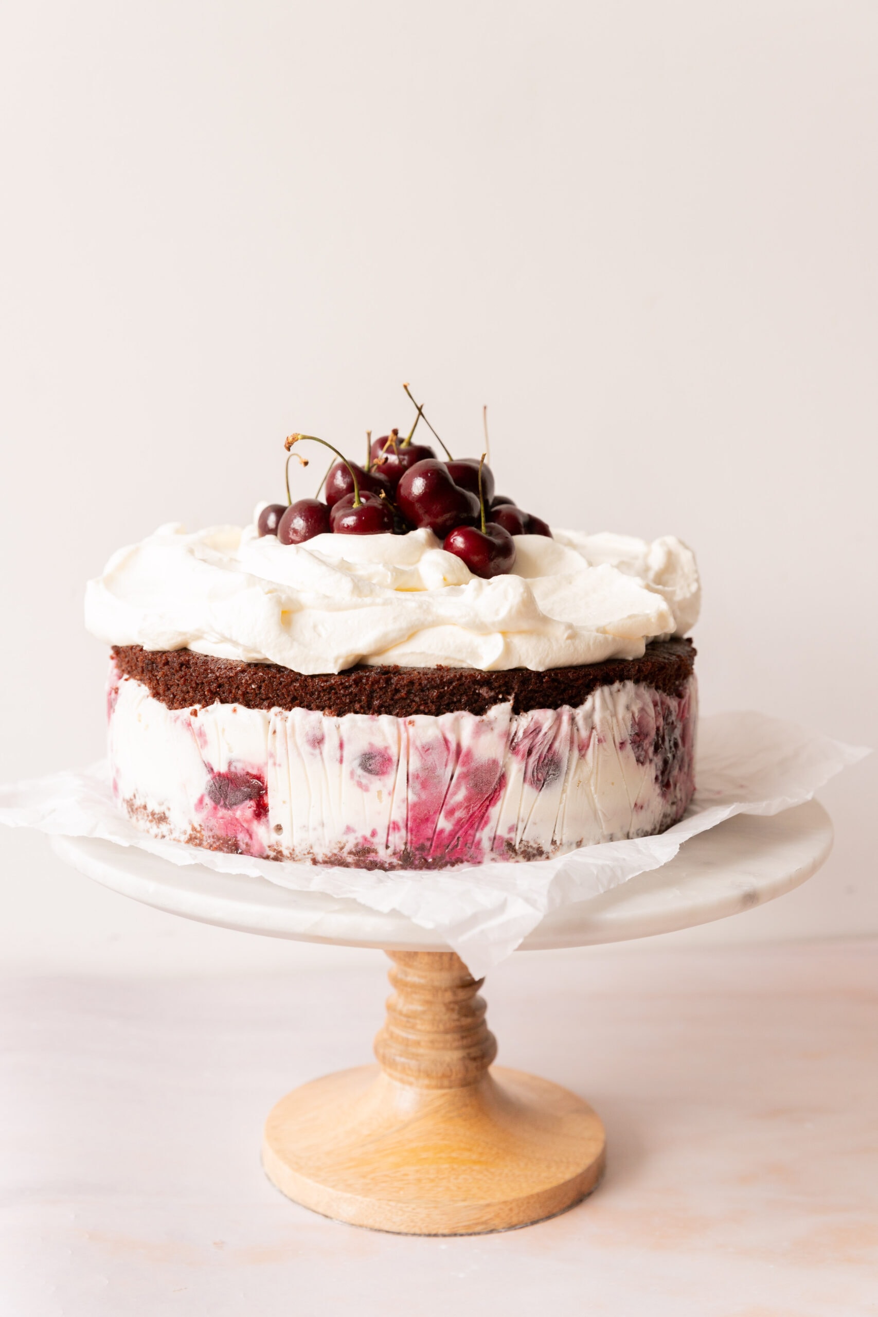 Side view of a black forest ice cream cake fully assembled on a cake stand lined with parchment paper. 