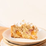 Side view of a slice of peach cake with oat streusel on a stack of plates.