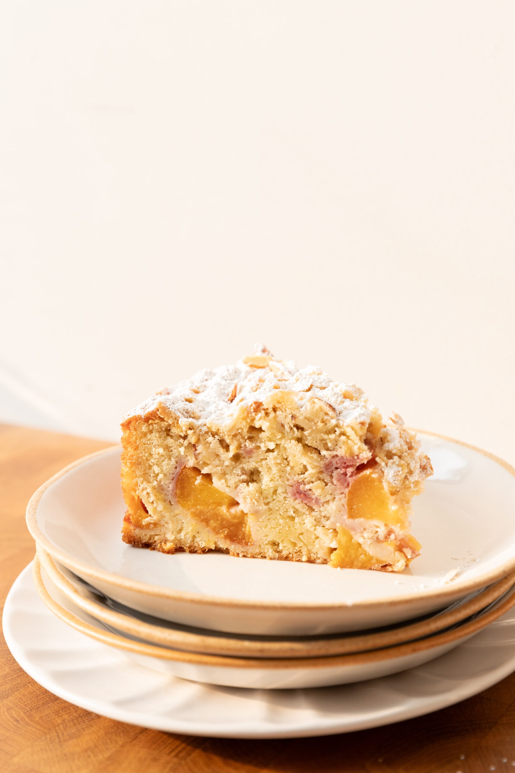 Side view of a slice of peach cake with oat streusel on a stack of plates. 