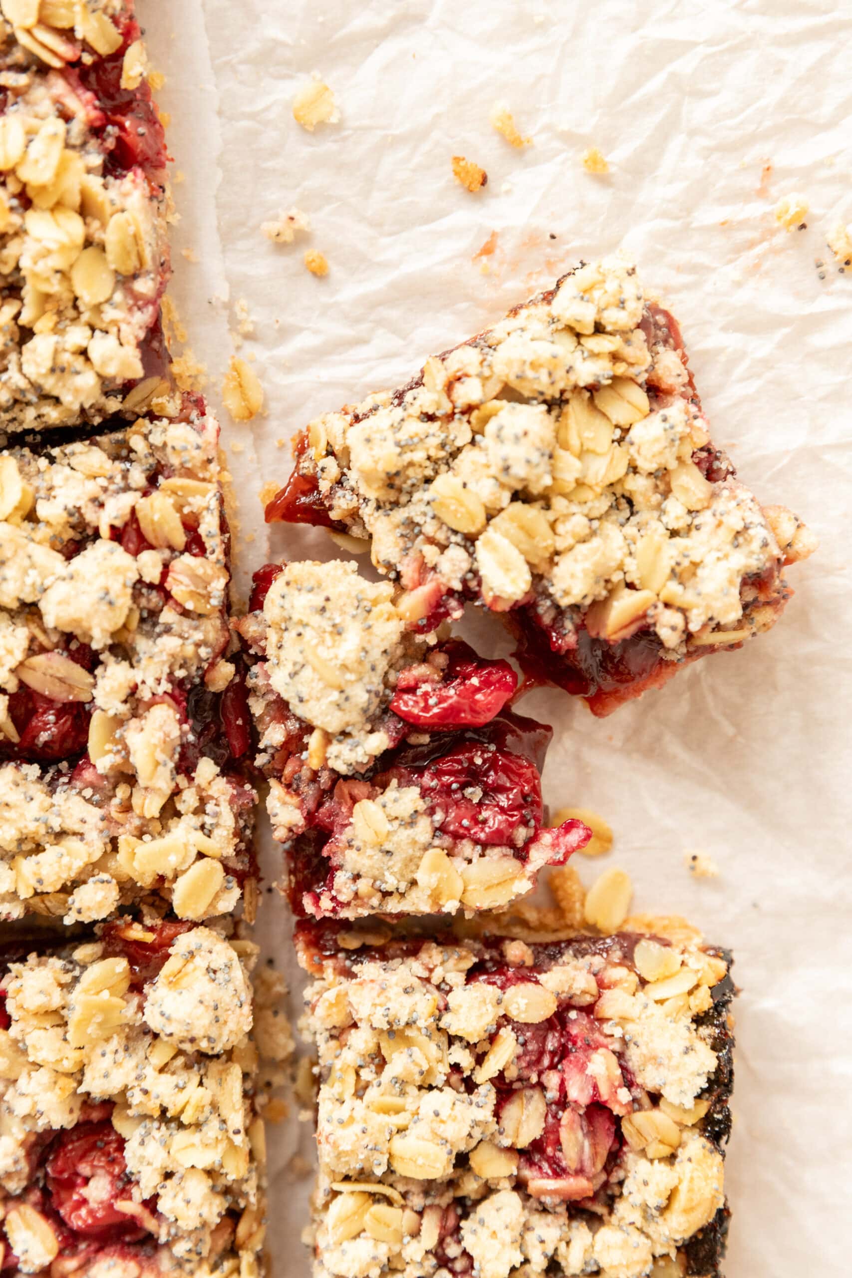 Overhead. view of plum bars with an oat and poppyseed streusel torn apart on white parchment. 