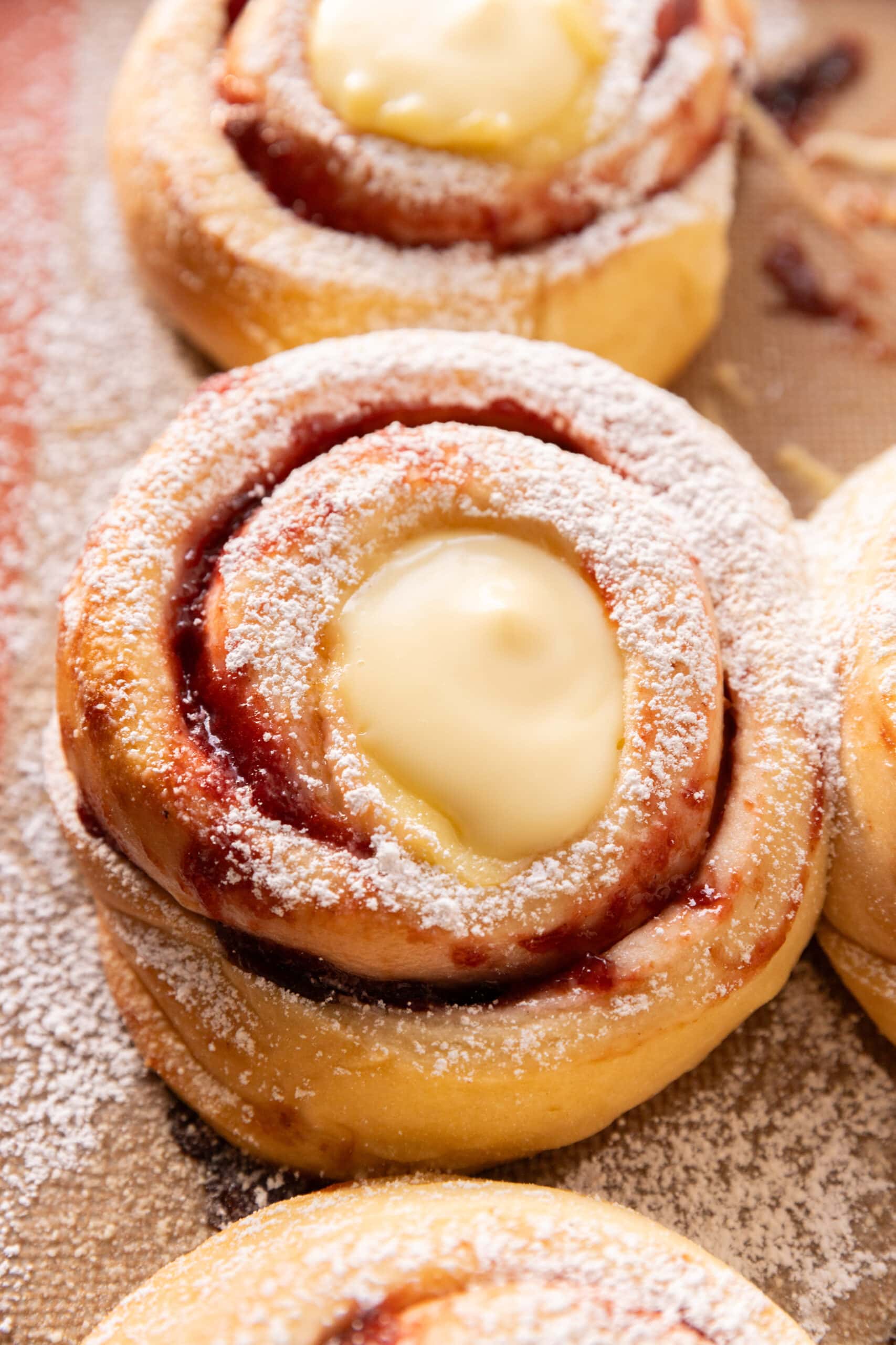 Angled view of German plum rolls, dusted with powdered sugar and topped with vanilla pudding.