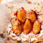 Angled view of a puff pastry plum tart with almond frangipane and a dusting of powdered sugar.