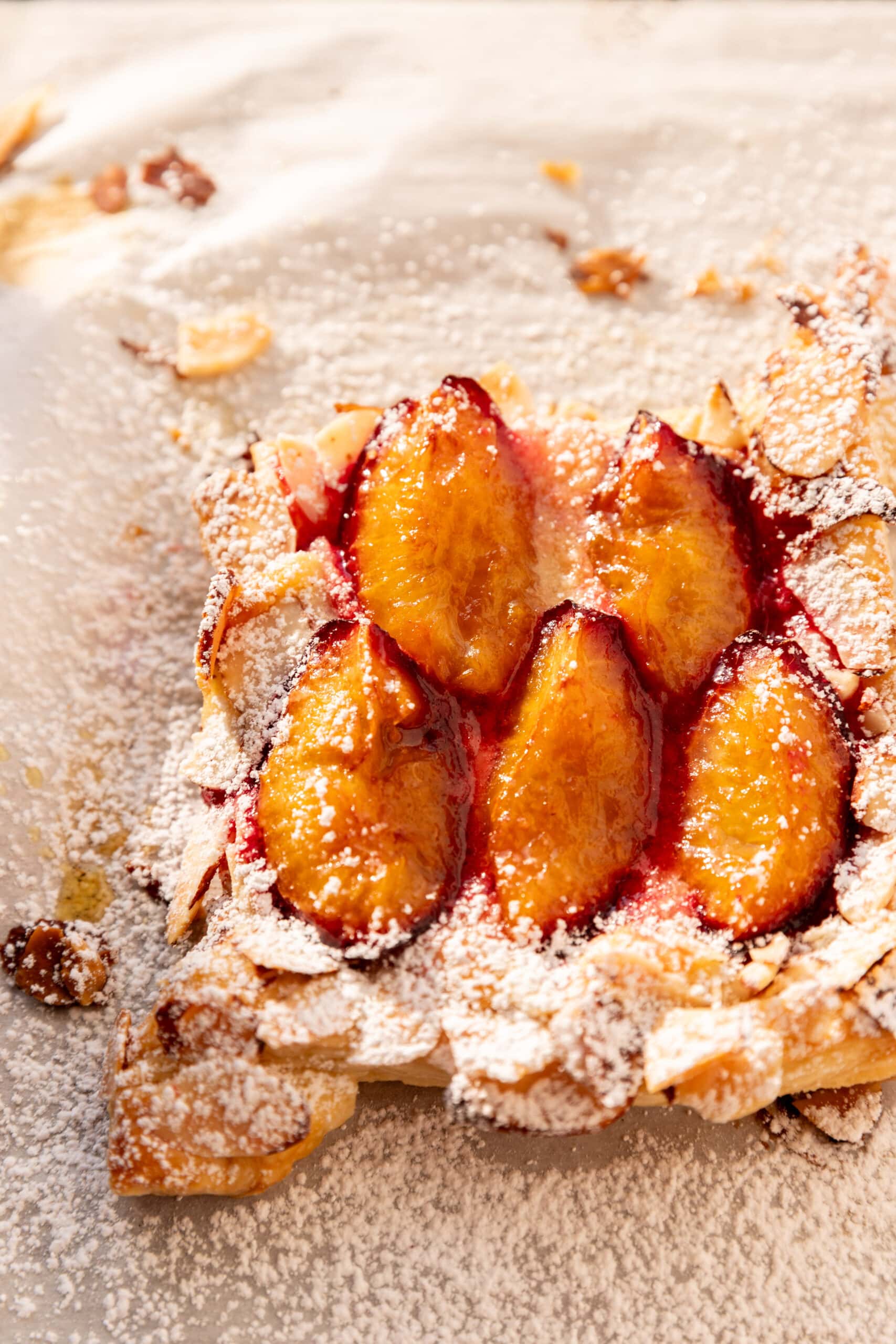 Angled view of a puff pastry plum tart with almond frangipane and a dusting of powdered sugar.
