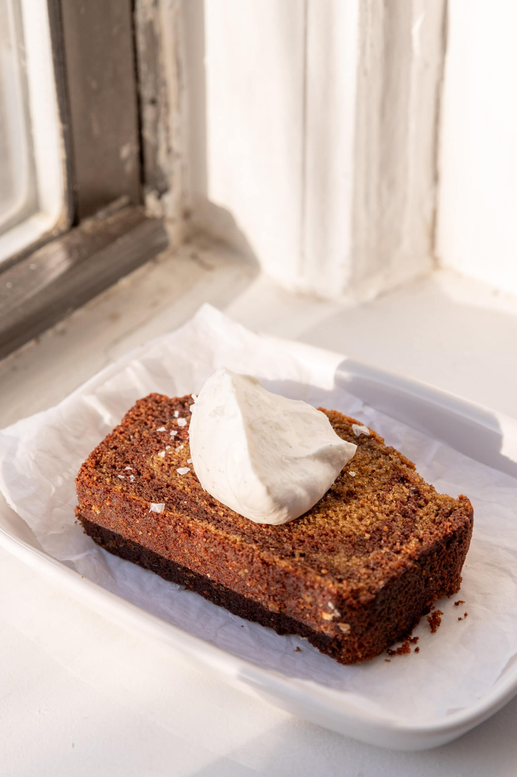 Slice of spiced marble loaf with nutmeg whipped cream sitting on a parchment lined plate.