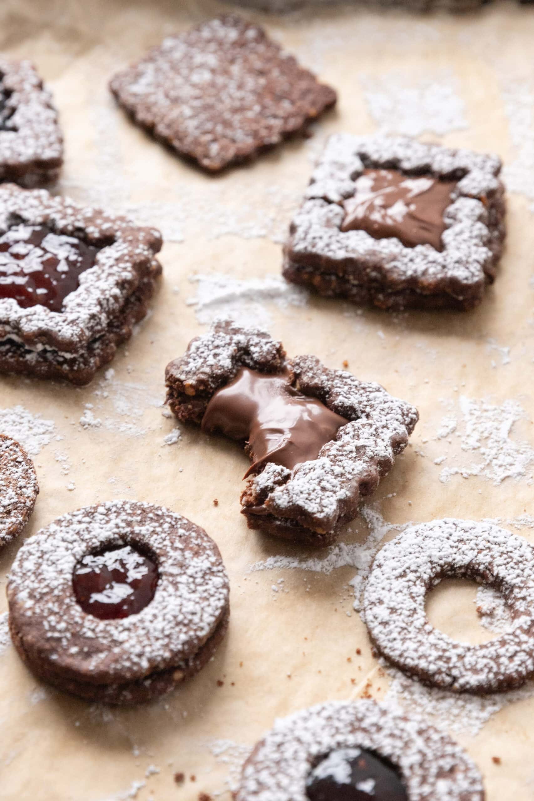 A parchment lined sheet pan topped with multiple Chocolate linzer cookies and one that has a bite taken out of it.