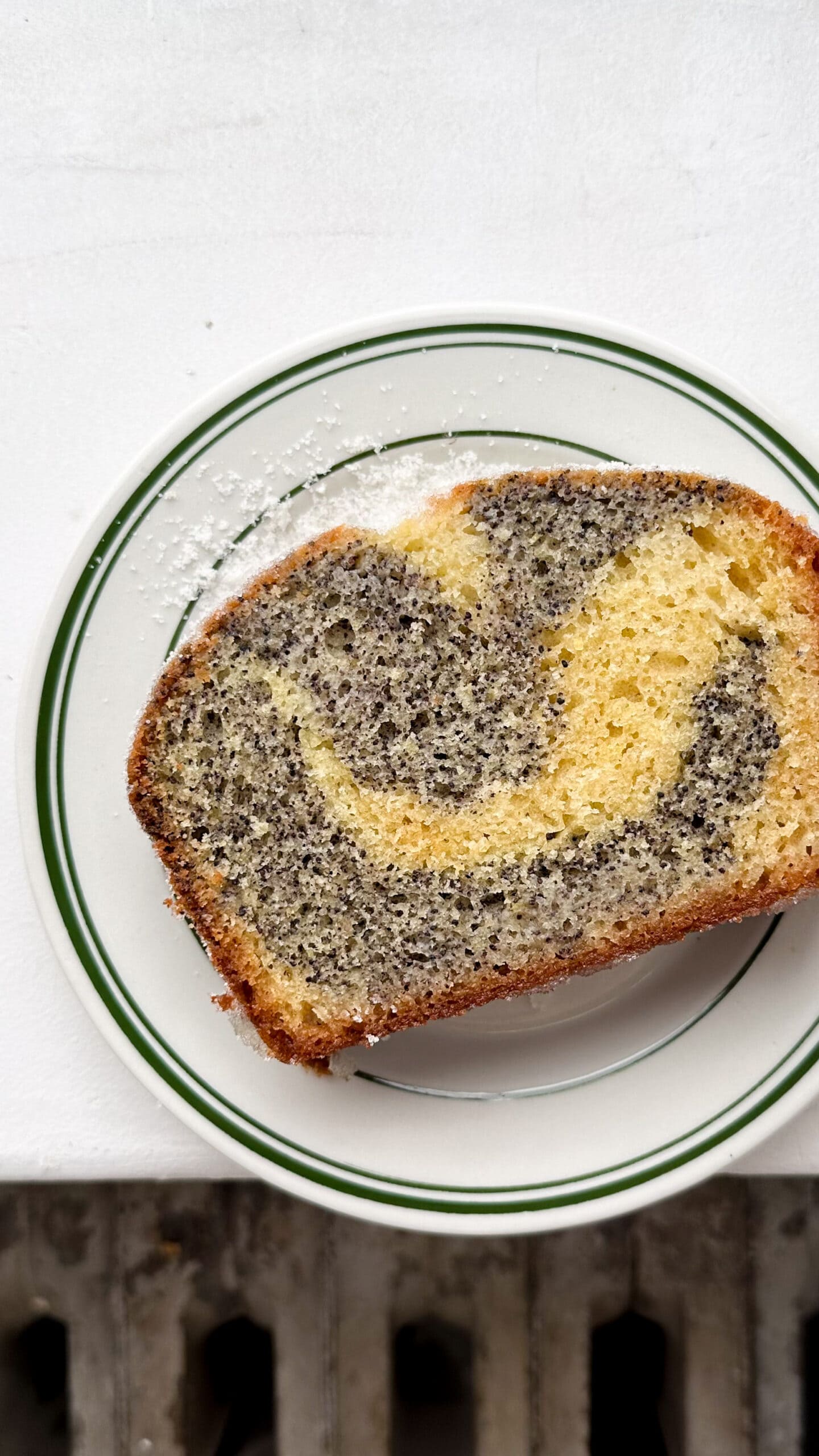 A slice of lemon poppyseed cake on a white and green plate. 