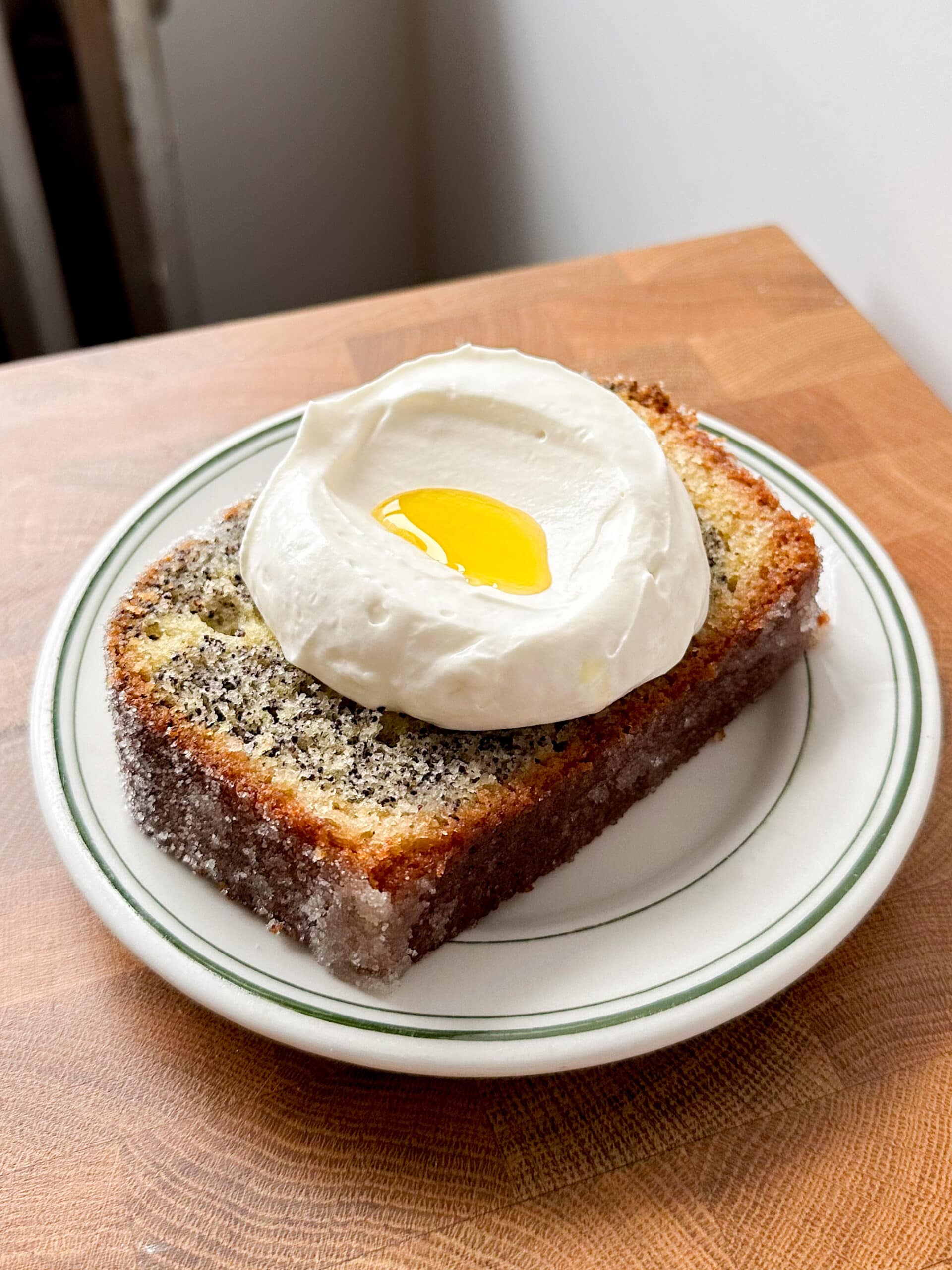 A slice of lemon poppyseed loaf cake topped with lemon yogurt whipped cream and a drizzle of olive oil. 