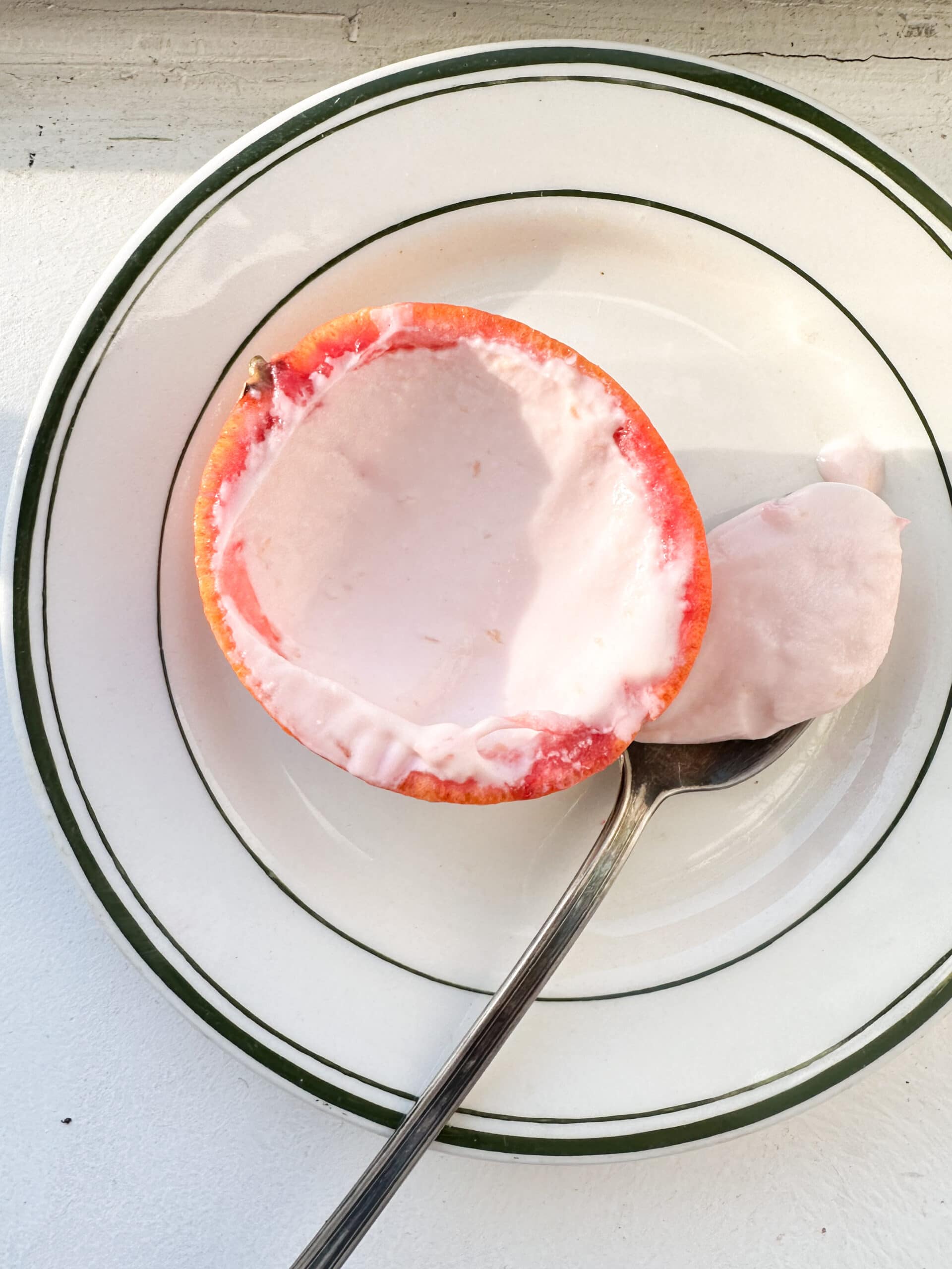 Overhead view of a blood orange posset with a spoonful taken out on a white and green plate.