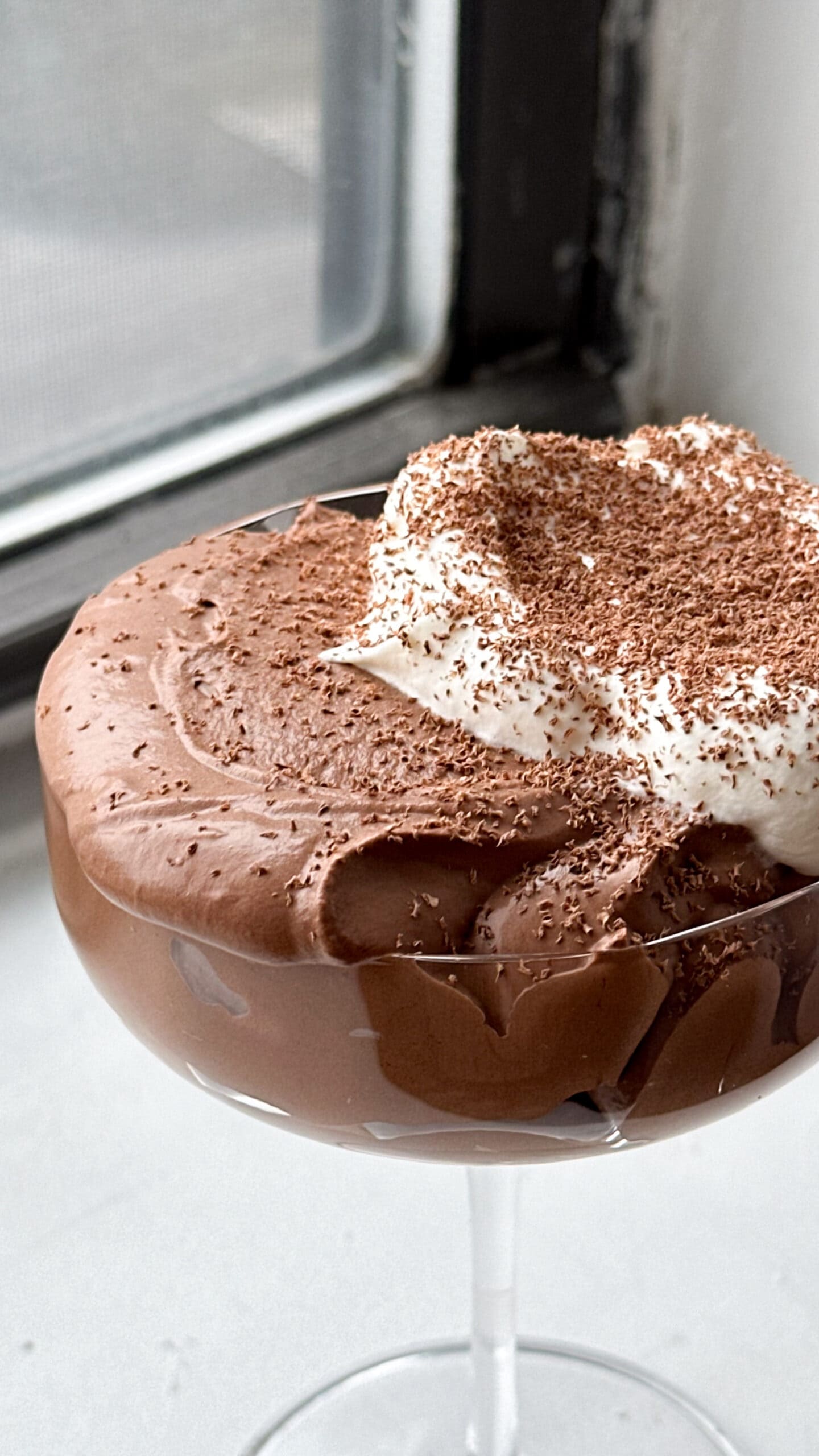 A coupe glass filled with dark chocolate mousse, topped with whipped cream, and sprinkled with grated chocolate. 