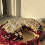 Berry Custard Cake with oat streusel on a parchment lined plate with a slice cut out.