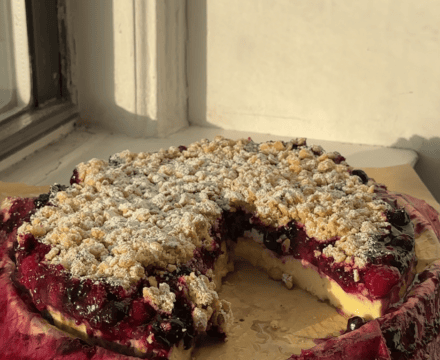 Berry Custard Cake with oat streusel on a parchment lined plate with a slice cut out.