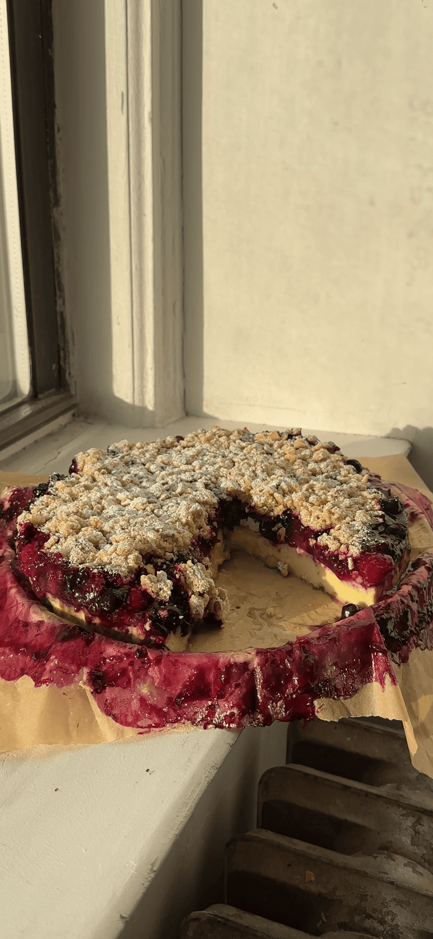 Berry Custard Cake with oat streusel on a parchment lined plate with a slice cut out.