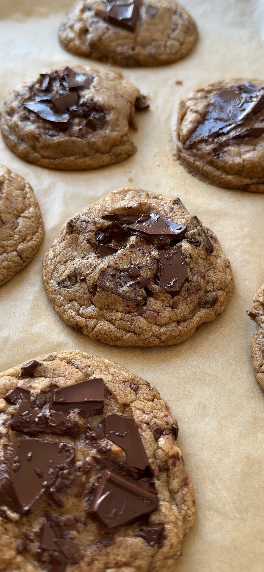 Chocolate chip cookies on a brown parchment lined baking sheet. 