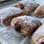 Cream and jam filled doughnuts, rolled in sugar on a baking sheet.