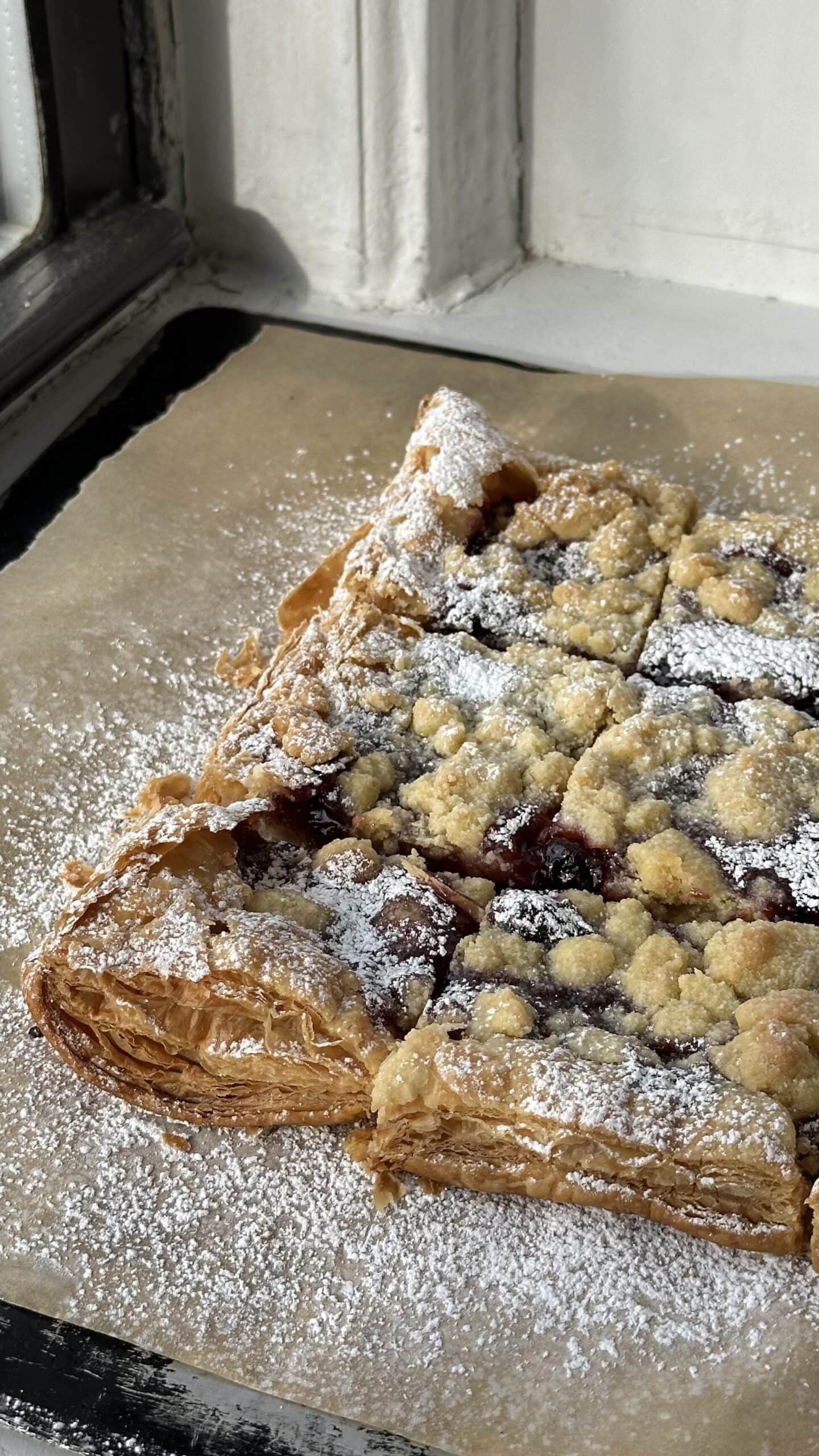Puff pastry, raspberry, and streusel bars on a parchment lined baking sheet dusted with powdered sugar.