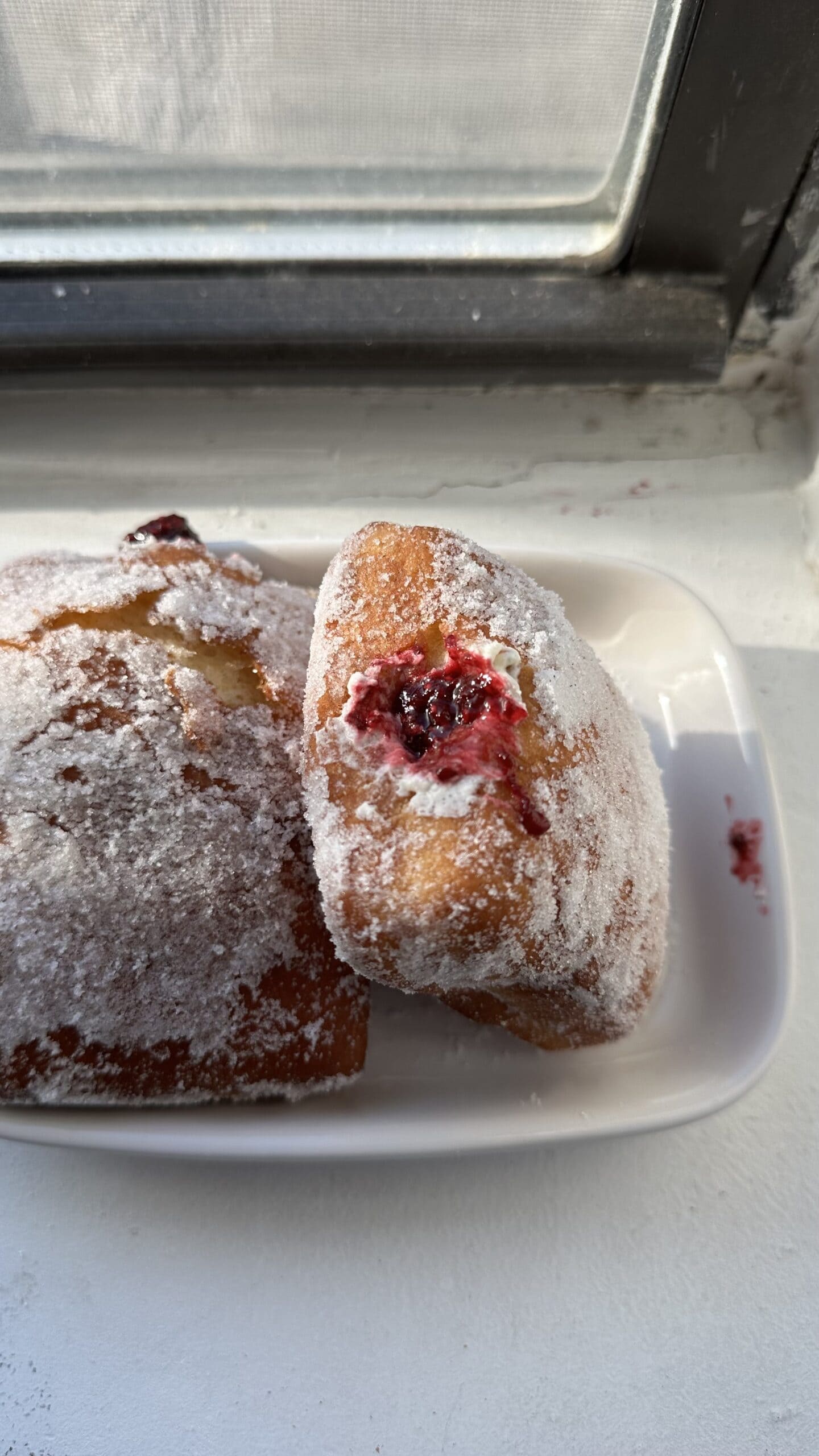Two sugar rolled, cream and jam filled doughnuts on a white plate.