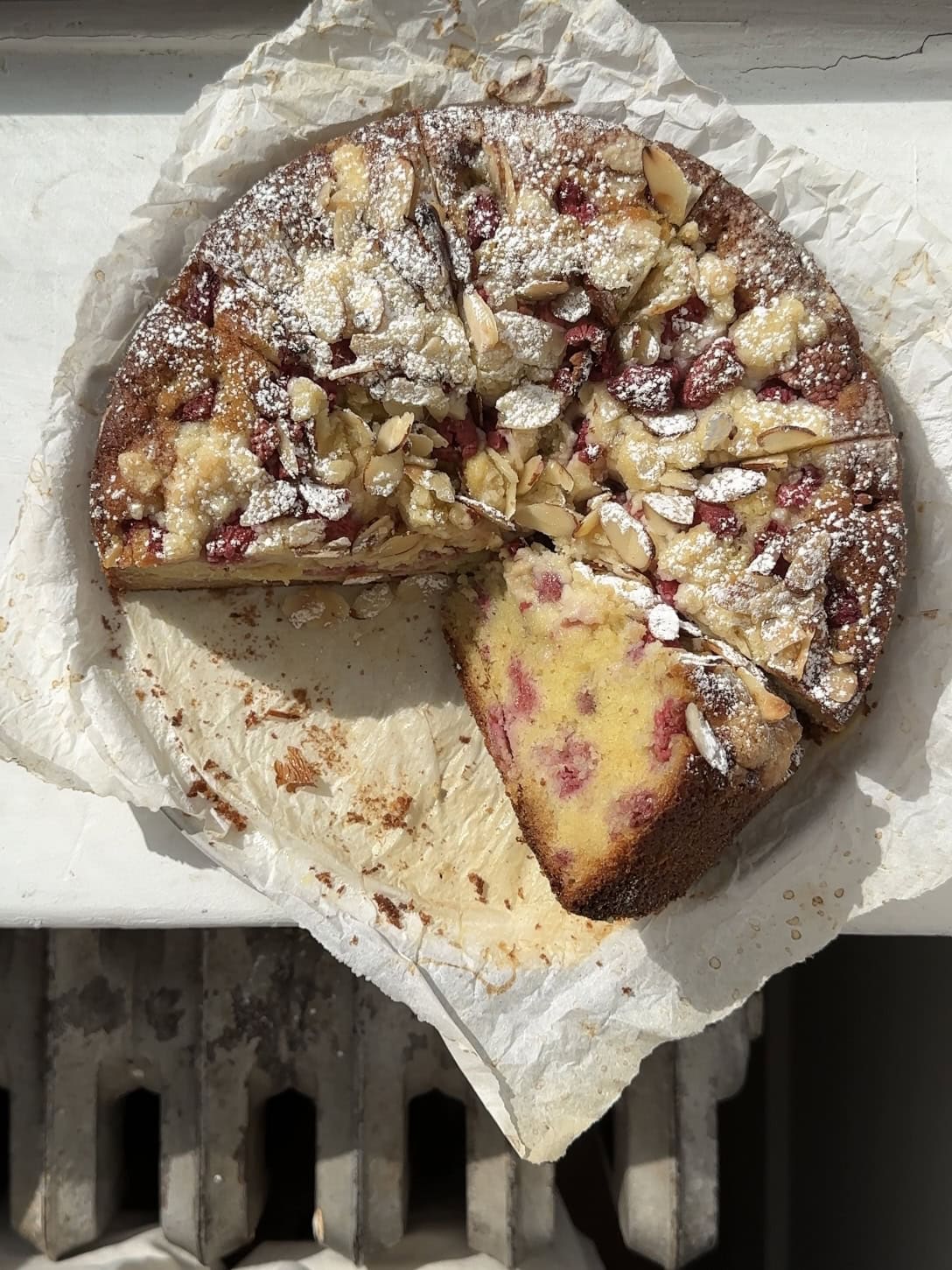 Overhead view of a raspberry almond coffee cake cut into slices on a sheet of parchment paper. 