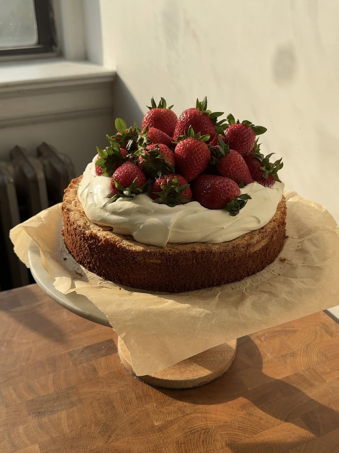 Side view of a Strawberries and Cream cake on a sheet of parchment paper on a cake stand. 