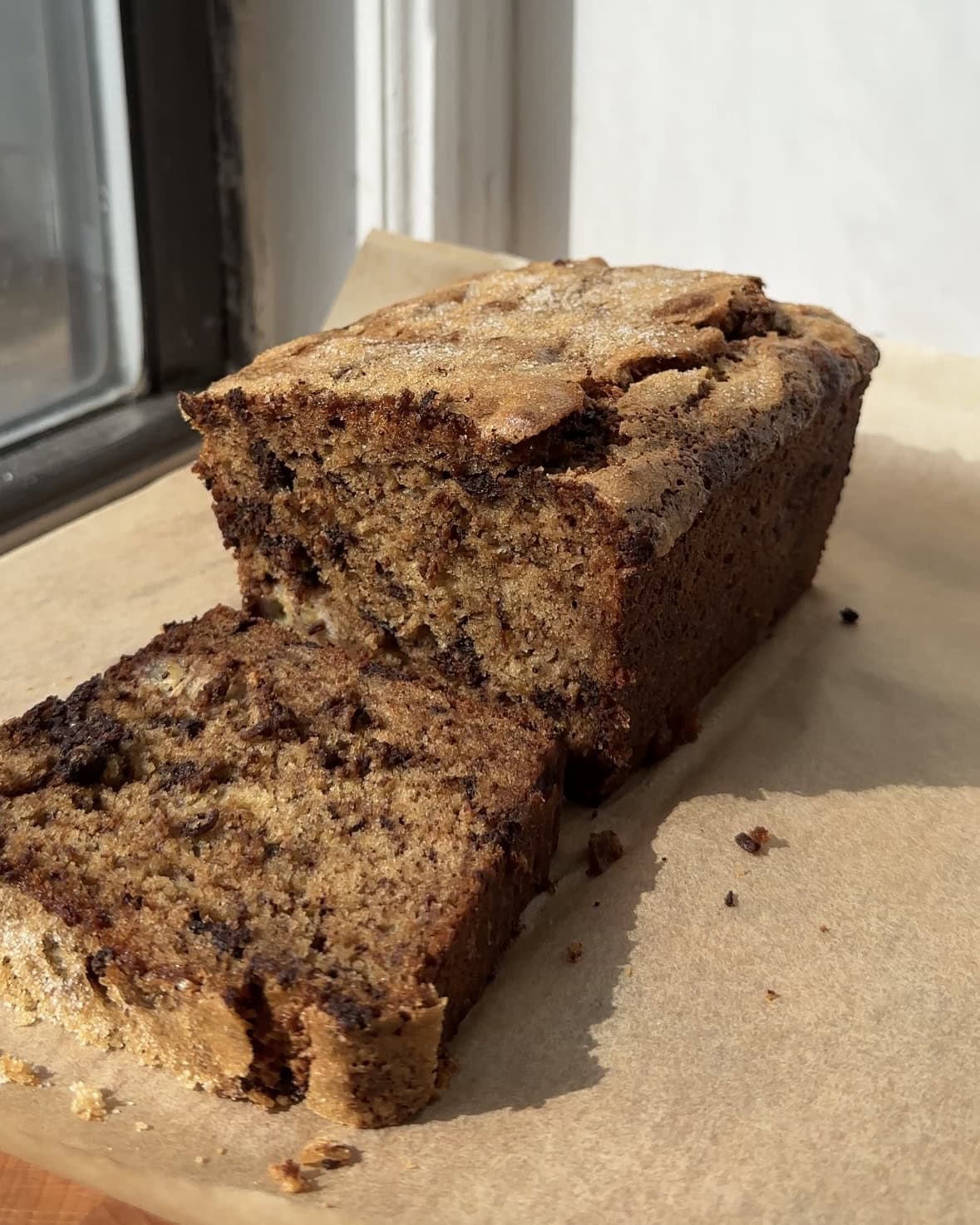 Side view of chocolate chunk banana bread on brown parchment paper with a slice cut.