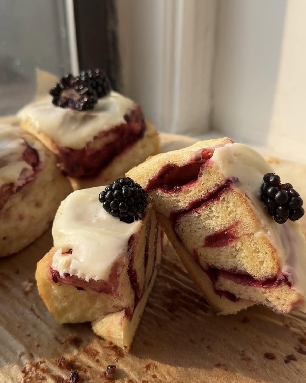 A lemon blackberry cinnamon roll with cream cheese frosting cut in half on brown parchment paper.