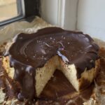 Side view of a feta cheesecake topped with melted chocolate and flaky salt with a slice cut out.