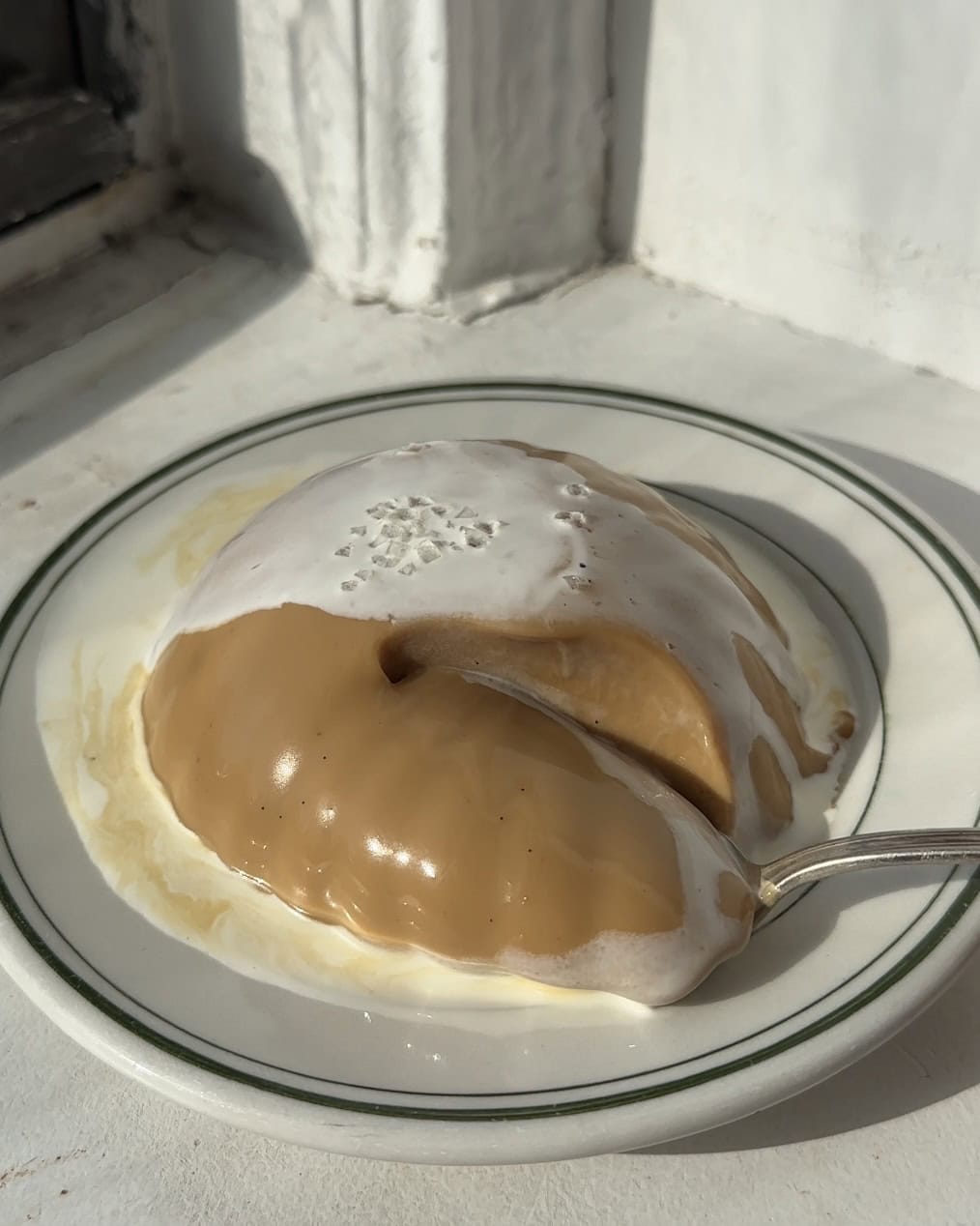 Side view of a burnt honey, white chocolate, espresso panna cotta on a small plate topped with heavy cream and flaky salt.