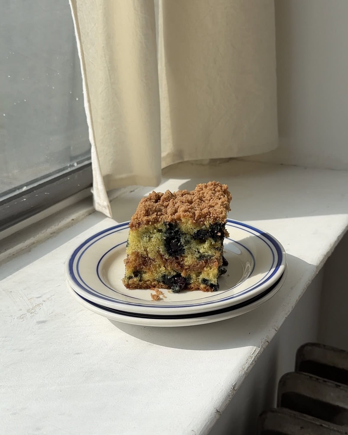 Side view of a slice of Blueberry Cinnamon Sugar Coffee cake on a white and blue plate.