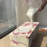 Side view of a Lemon Berry Ice Cream cake being glazed with a lemon glaze.