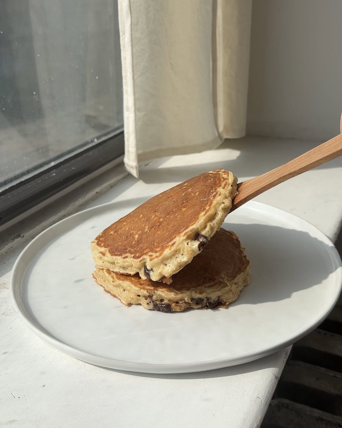 Side view of one oatmeal chocolate chip pancake being stacked on top of another.