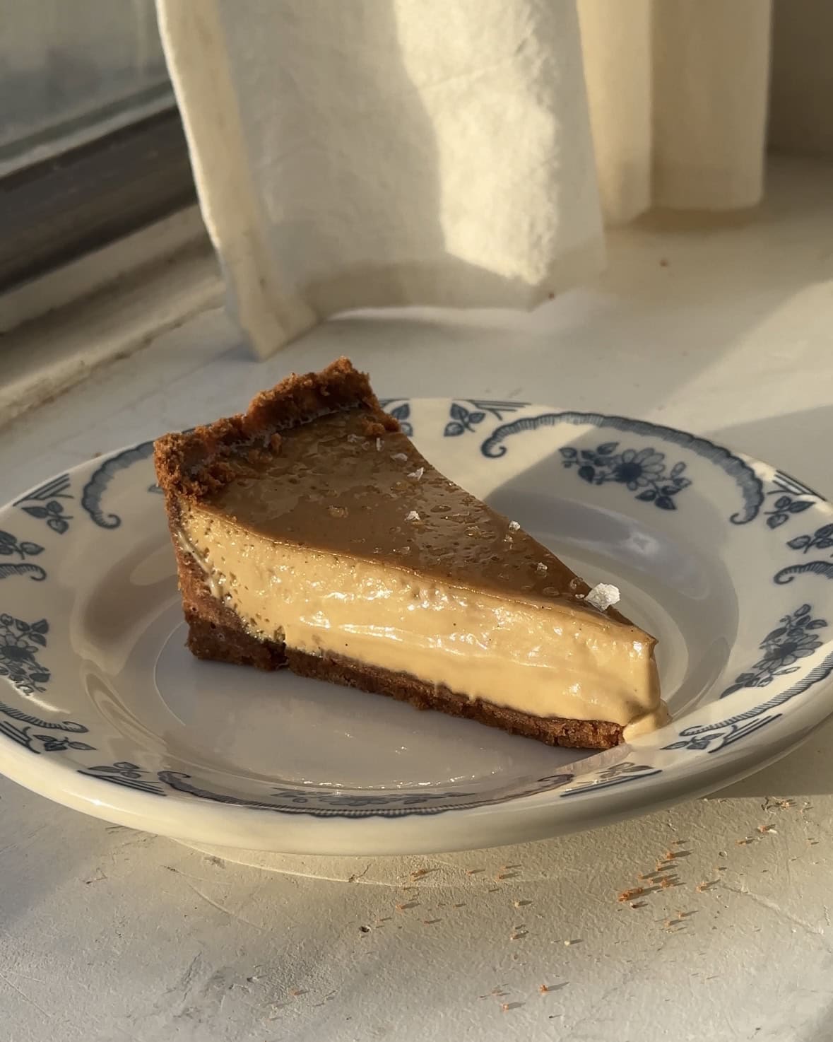 Side view of a slice of a Maple Sea Salt Latte Custard Tart on a blue and white plate.