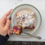 Overhead view of a cranberry crumb cake with a bite taken out showing the layers on a white and green plate.
