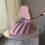 Side view of a Berry Yogurt Panna cotta in the shape of a bundt pan on a glass cake stand.