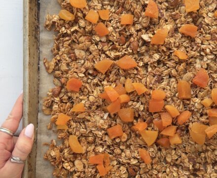 Overhead view of a Honey Almond Granola on a baking sheet topped with chopped dried apricots.