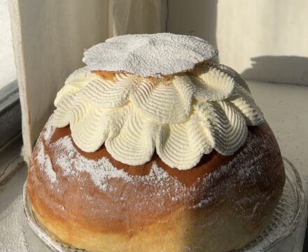 Side view of a Raspberry Semla Cake on a crystal plate dusted with powdered sugar.
