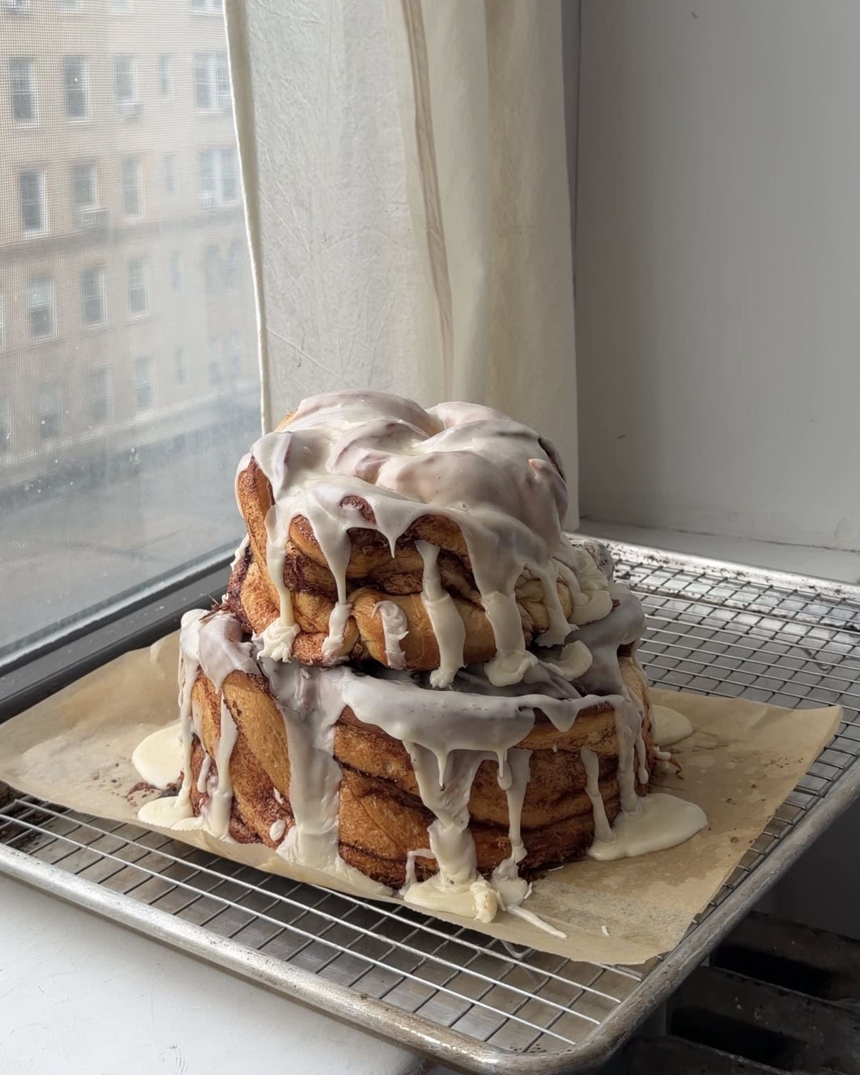 Two tiered cinnamon roll cake stacked together on a wire rack with frosting dripping over the edges.
