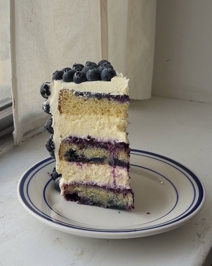 Side view of a slice of lemon blueberry cake with a lemon cream cheesecake filling.