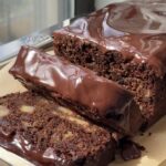 Side view of a double chocolate banana bread topped with a chocolate ganache and slices cut showing the banana chunks.