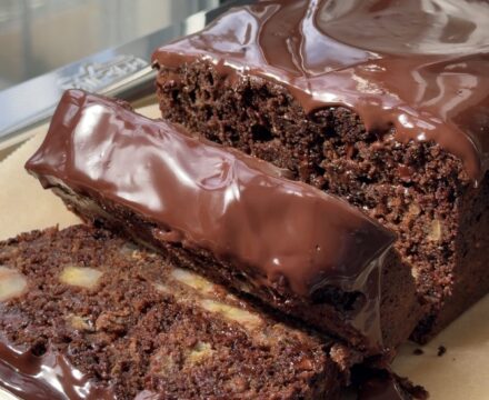 Side view of a double chocolate banana bread topped with a chocolate ganache and slices cut showing the banana chunks.