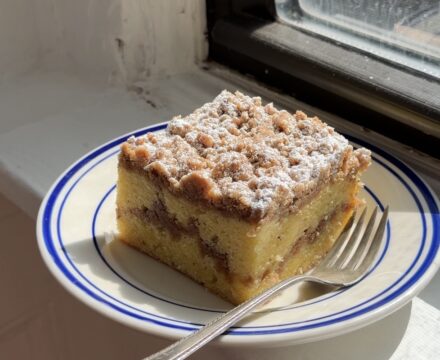 Side view of a large slice of sour cream coffee cake on a white and blue plate.