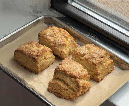 Side view of a baking sheet with four sea salt buttermilk biscuits.