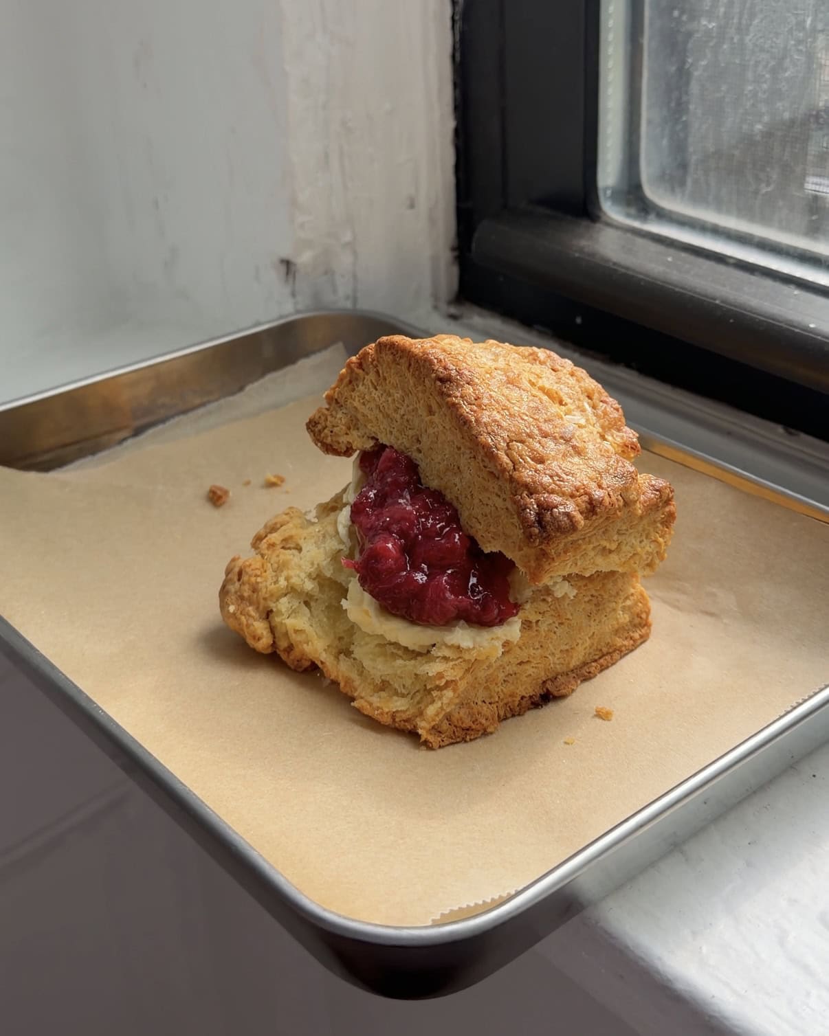 Side view of a buttermilk biscuit with butter and strawberry jam.