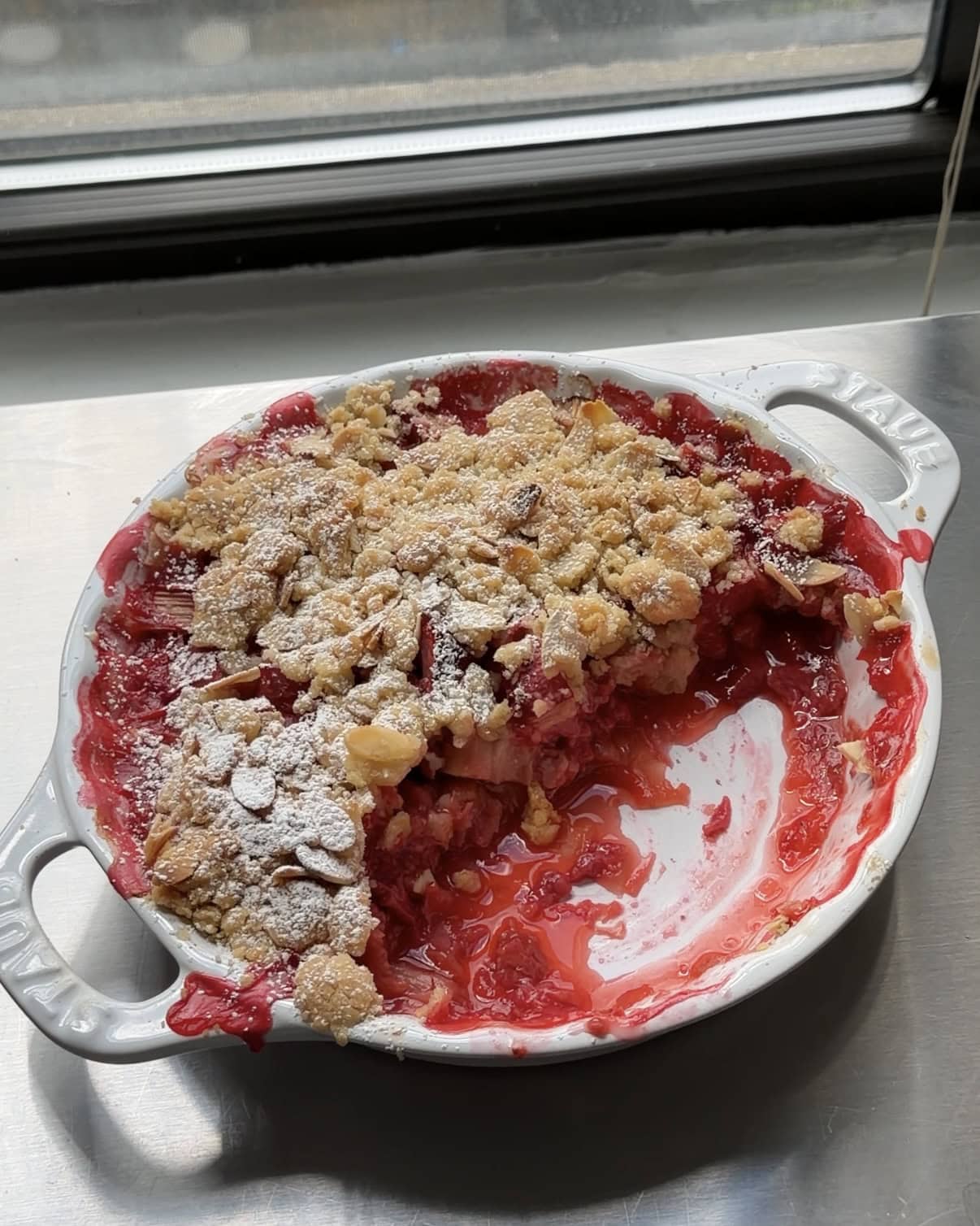 Overhead view of a rhubarb crumble with some scooped out of the baking dish.