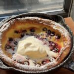 Overhead view of a lemon blueberry dutch baby in a cast iron pan topped with whipped cream and powdered sugar.