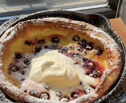 Overhead view of a lemon blueberry dutch baby in a cast iron pan topped with whipped cream and powdered sugar.
