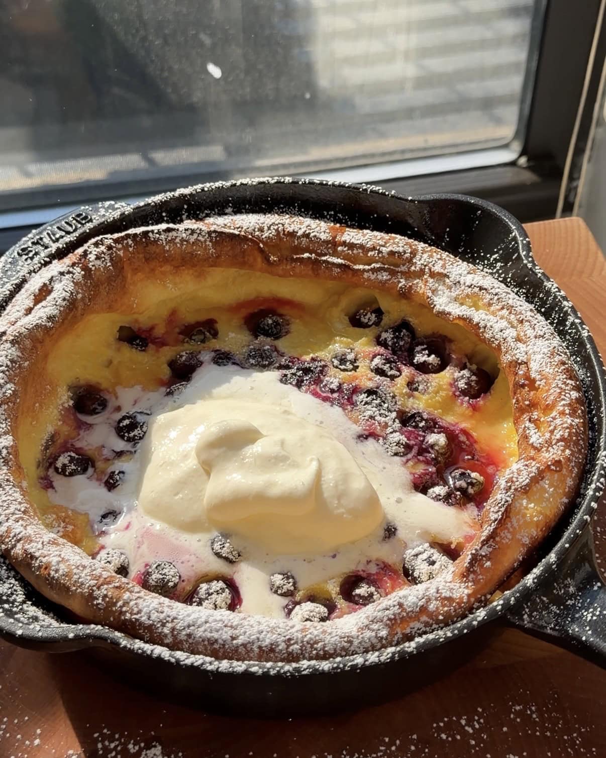 Overhead view of a lemon blueberry dutch baby in a cast iron pan topped with whipped cream and powdered sugar.