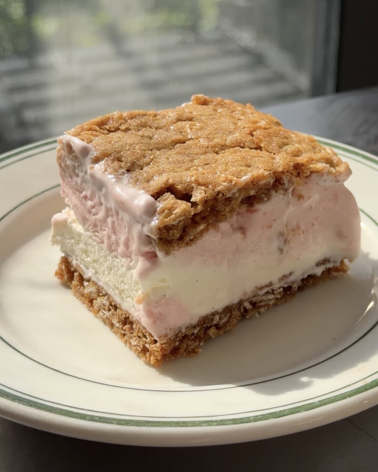 Side view of a Strawberry Ice Cream Oatmeal Cream Pie sandwich on a white and green plate.