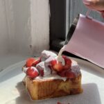 Side view of a thick slice of Brioche French toast topped with strawberries and chamomile cream.