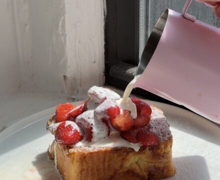 Side view of a thick slice of Brioche French toast topped with strawberries and chamomile cream.