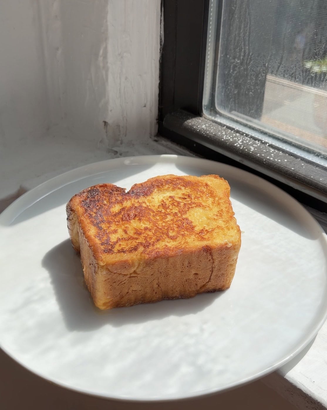 Side view of a slice of Brioche French toast with no toppings on a big white plate.