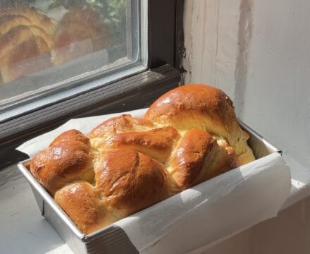 Side view of a Classic Brioche loaf in a metal pan on a window sill.